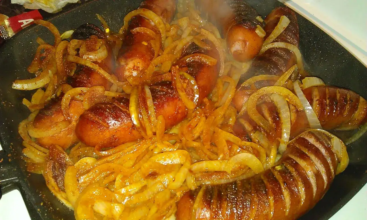 Pyszna kiełbasa z piekarnika duszona z cebulką, parująca i apetyczna.