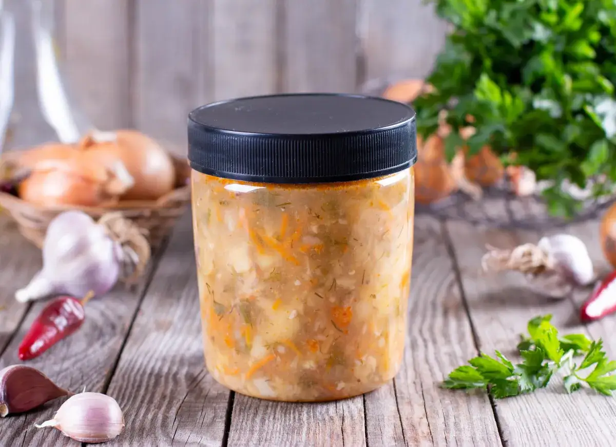 Słoik z gotową zupą, idealny do zamrożenia. Obok składniki: cebula, czosnek, papryczka chili i natka pietruszki.
