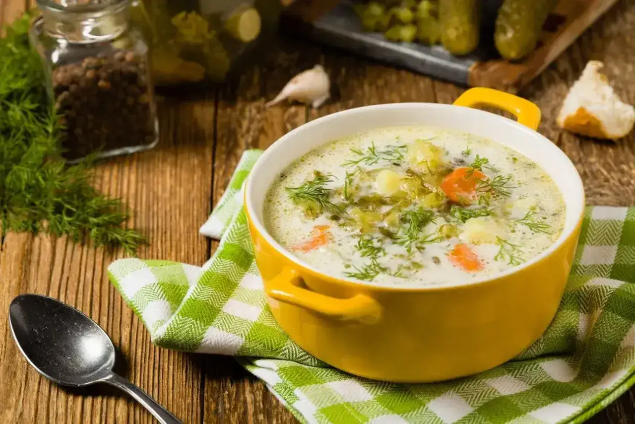 Zupa ogórkowa z koperkiem i ziemniakami. W tle słoik z pieprzem, czosnek i ogórki kiszone – idealne jakie przyprawy do zupy ogórkowej.