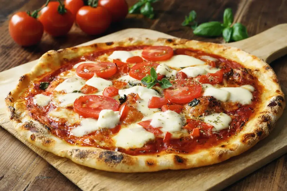 Pyszna pizza capricciosa z pomidorami i mozzarellą, ozdobiona świeżą bazylią, na drewnianej desce.