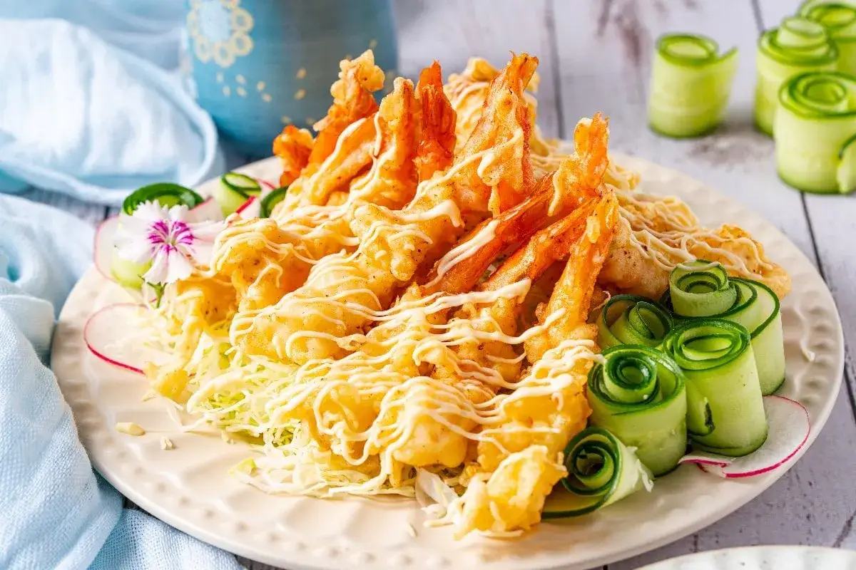 Chrupiące krewetki w cieście tempura, polane majonezem, podane z poszatkowaną kapustą i ozdobnymi rolkami z ogórka. Pyszne tempura co to jest, już wiesz!