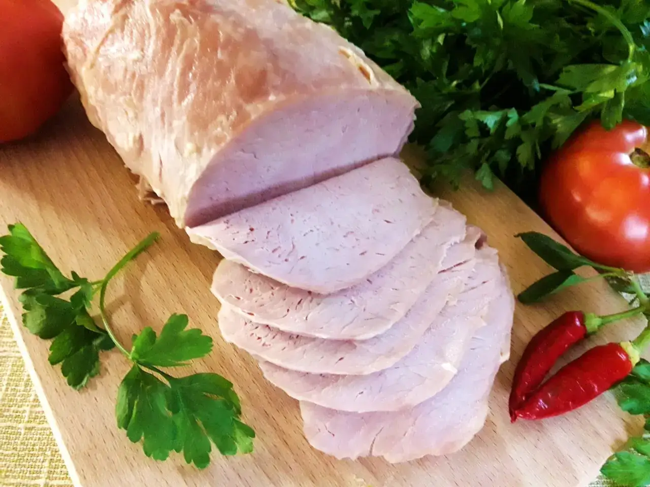 Super delikatny i soczysty schab gotowany, pokrojony w plastry, z pomidorami, papryczkami chili i natką pietruszki na desce.