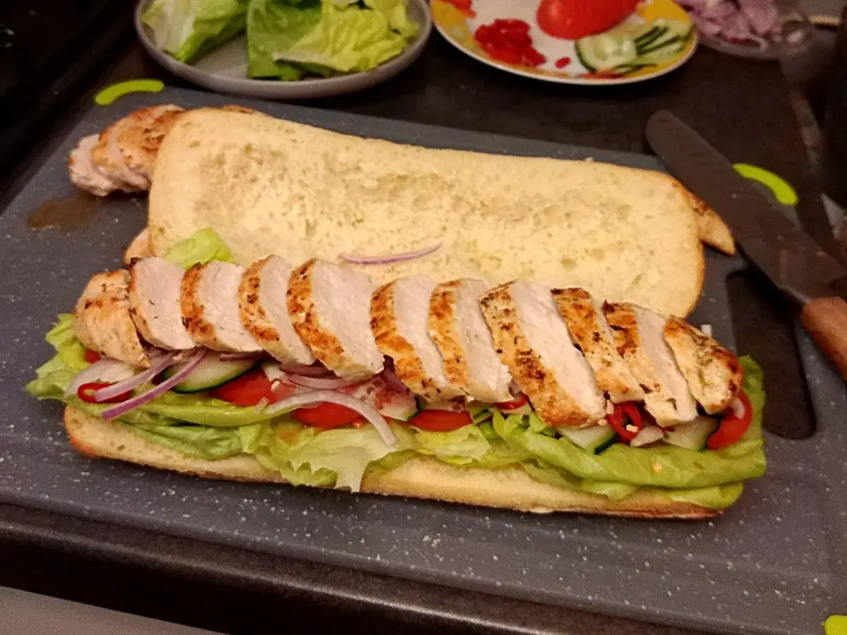 Pyszne panini z kurczakiem, sałatą, pomidorem i ogórkiem na świeżej bułce. Idealne na szybki lunch.