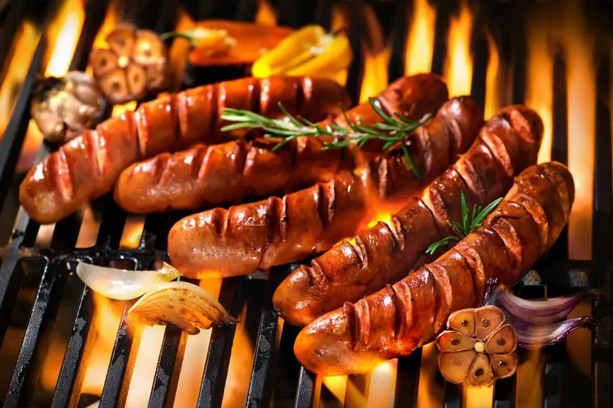 Aromatyczna kiełbasa z grilla skwierczy na ruszcie, otoczona płomieniami. Obok pieczona cebula i czosnek dodają smaku.