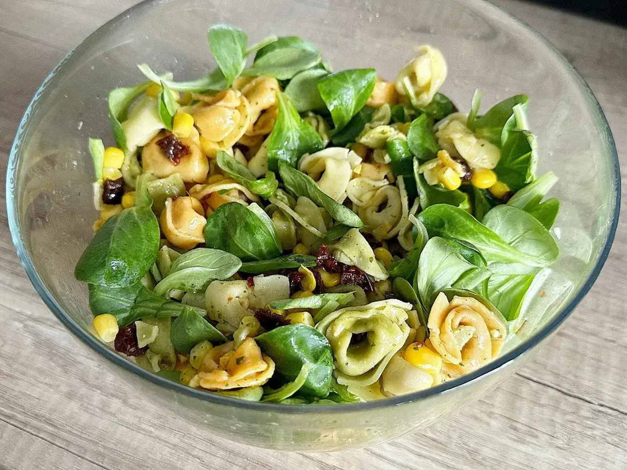 Najlepsza sałatka z tortellini: kolorowe pierożki, kukurydza, suszone pomidory i świeża sałata w szklanej misce.