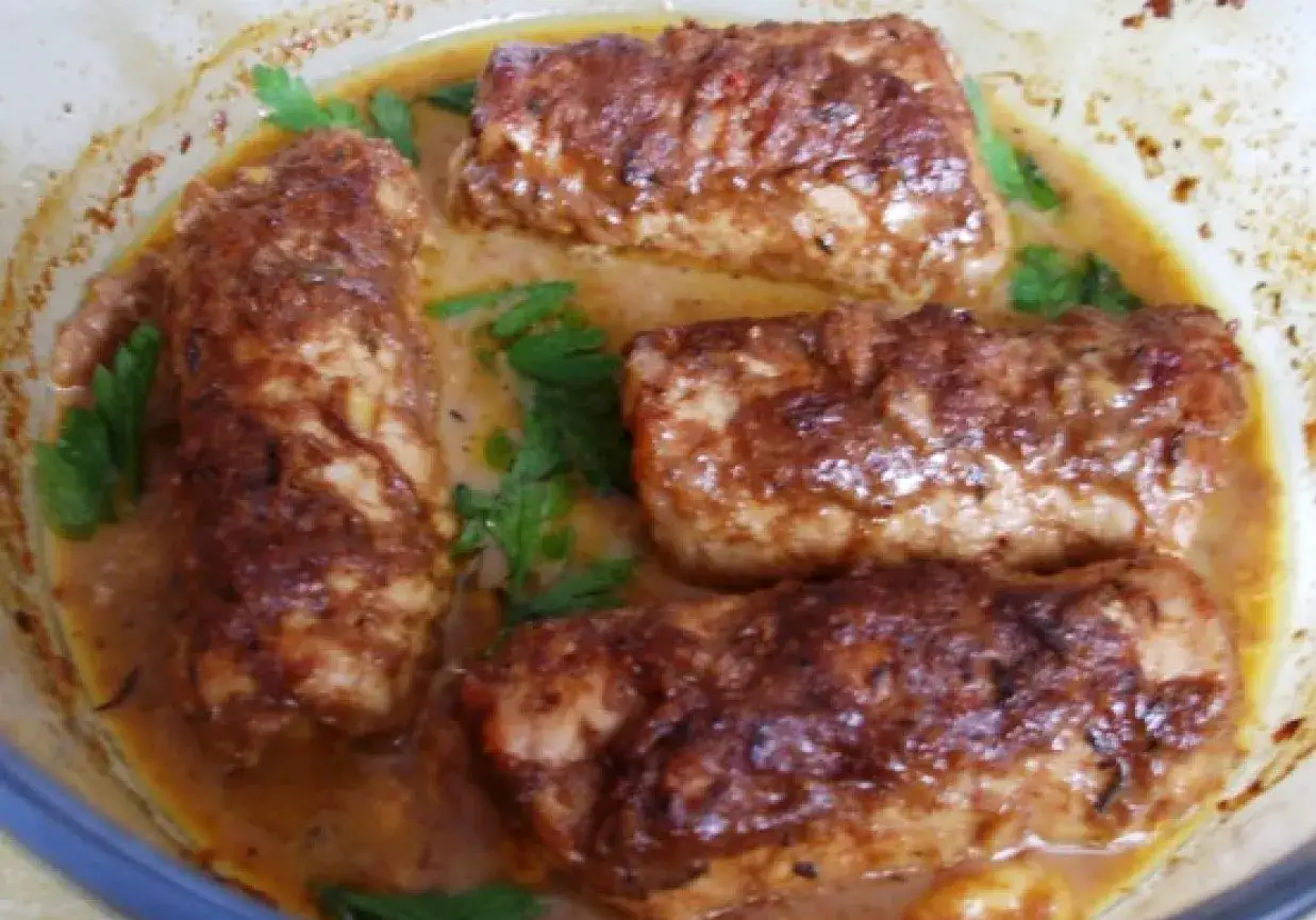 Roladki schabowe pieczone w naczyniu, zanurzone w aromatycznym sosie, ozdobione zieloną pietruszką.