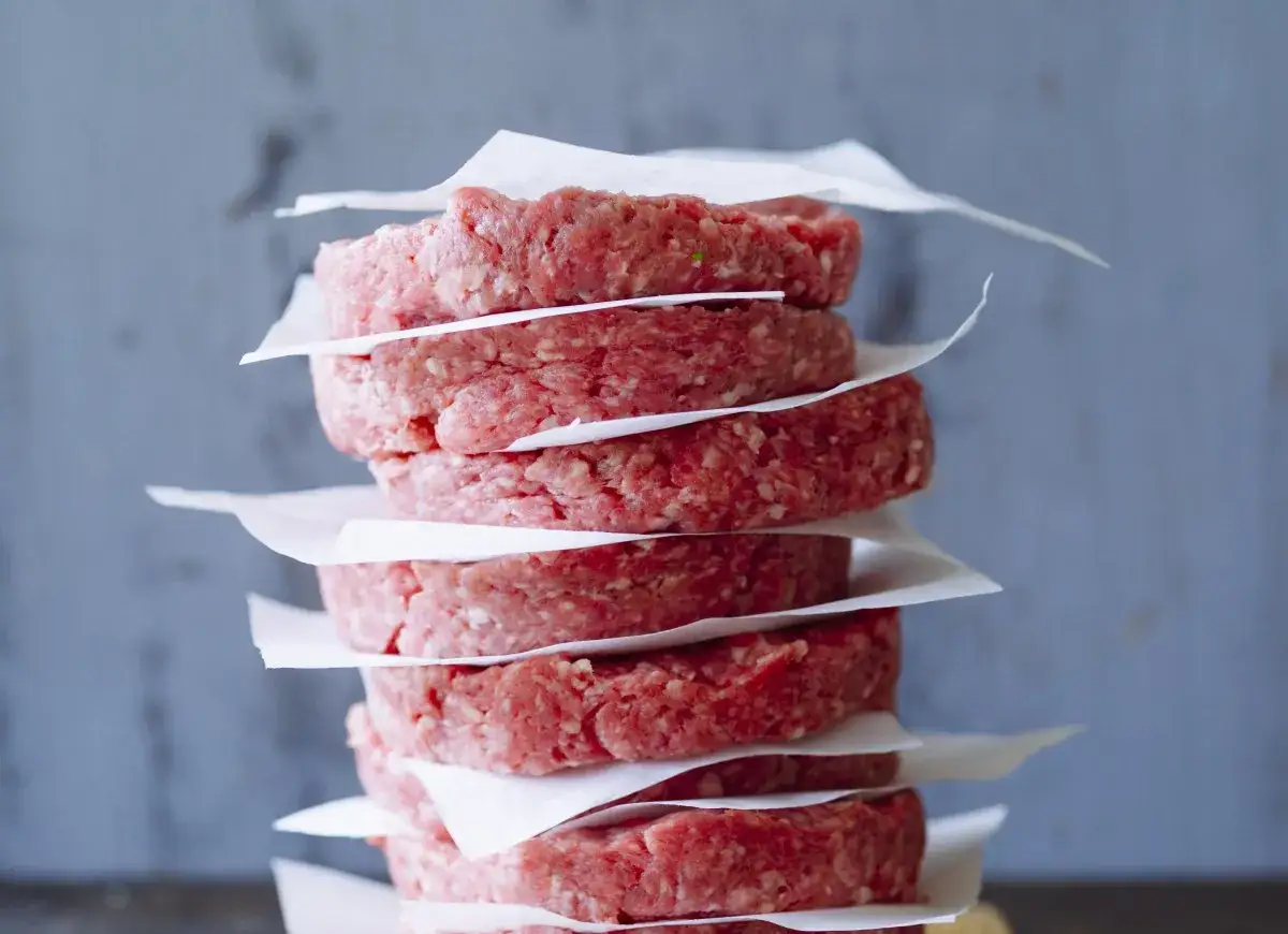 Stos surowych kotletów na hamburgery, każdy oddzielony papierem. Idealne do eksperymentowania, jak przyprawić mięso na hamburgery.
