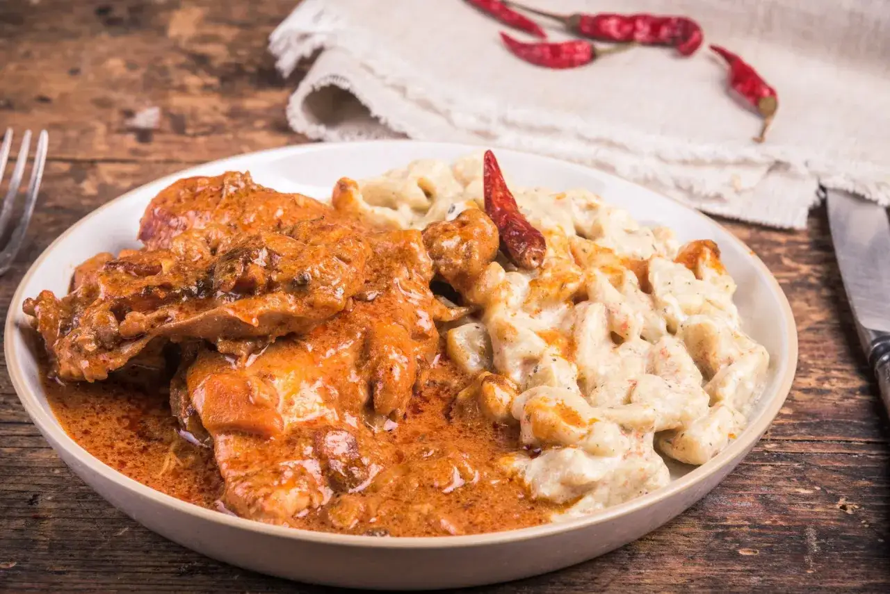 Danie z kurczaka w sosie pomarańczowym i kremowym, ozdobione suszonymi bitkami chili.