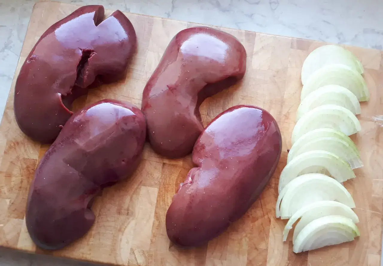 Ania gotuje cynaderki. Na desce leżą cztery surowe cynaderki i pokrojona w krążki cebula, gotowe do przyrządzenia pysznego dania.