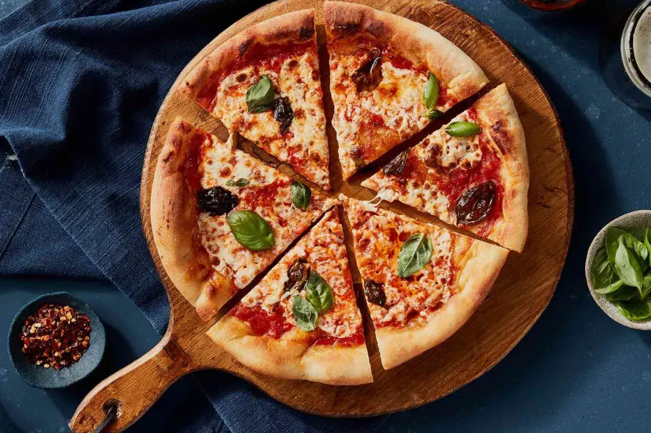Pyszna margarita pizza z bazylią i pomidorami, pokrojona na kawałki, na drewnianej desce.