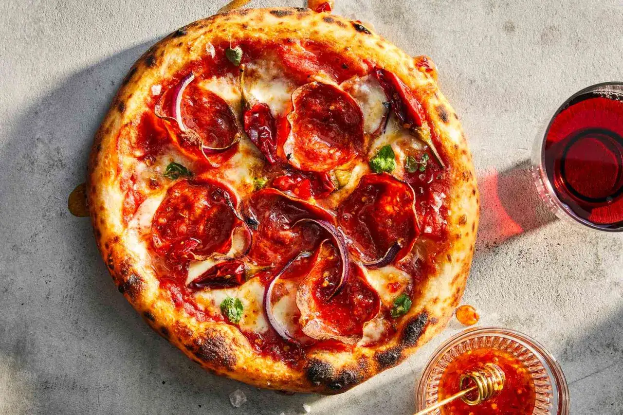 Idealny dzień pizzy: gorąca pizza z pepperoni, cebulą i chili, obok kieliszek czerwonego wina i miseczka miodu z chili.