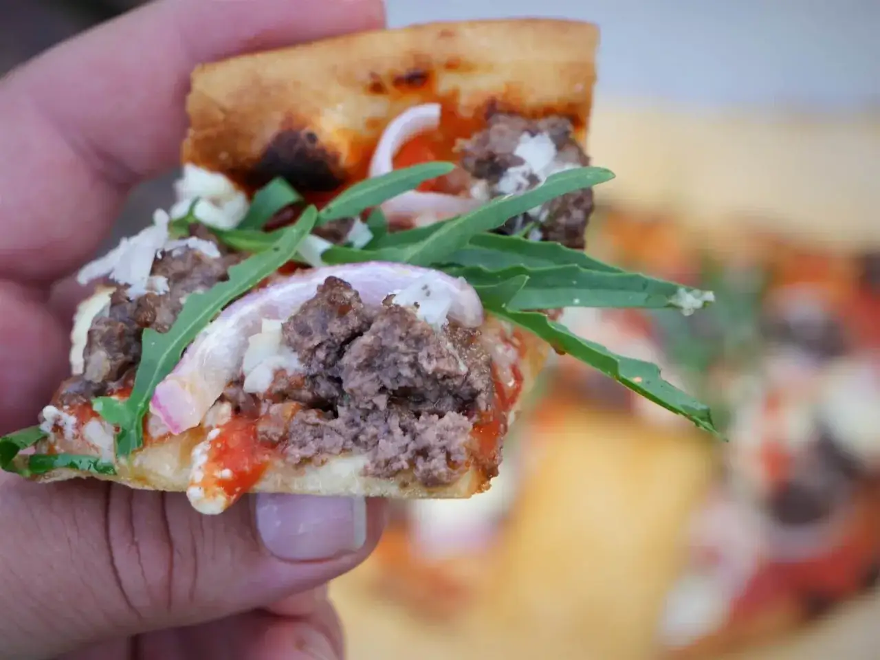 Kawałek pizzy z mielonym mięsem, czerwoną cebulą i rukolą. Zastanawiasz się, ile kalorii ma pizza 30 cm?